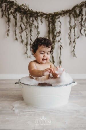 A baby girl plays in a bubble bath after her cake smash session