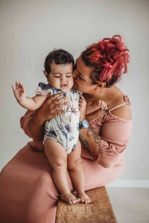 A mother sits with her baby girl on a timber bench for a milestone photo