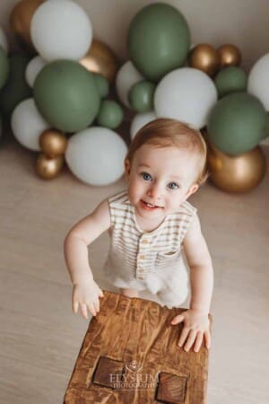 A little boy smiles as he walks in front of balloons during his cake smash session