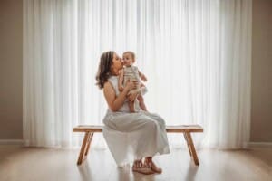 A mother sits on a bench with her baby boy in her lap cuddling him