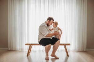 A dad cuddles his baby boy who is sitting on his lap in a studio