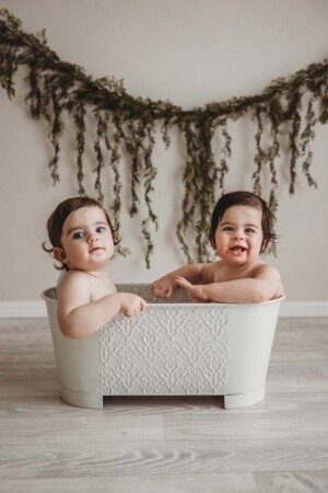 Twin baby boys sit in a white vintage bathtub to clean up after their cake smash session