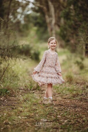 A little girl in a floral dress spins around dancing in a grassy field