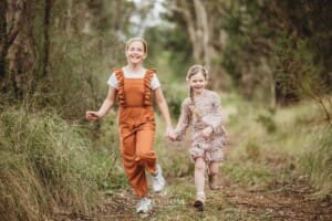 Two girls hold hands as they run along a bush track