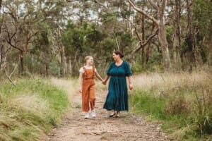 A mother and daughter hold hands as they walk along a bush track