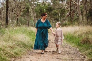 A mother holds hands with her little girl as they walk along a track in a grassy field