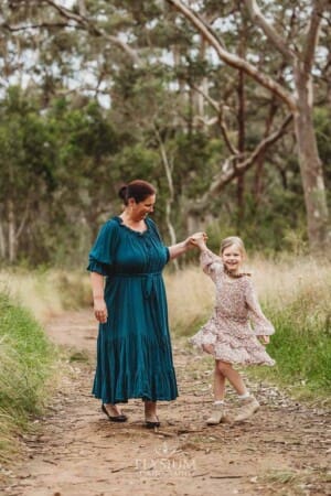 A little girl holds her mothers hand and twirls around in a grassy field
