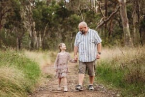 A father walks along a bush track with his little girl holding hands