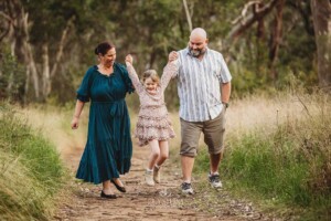 Parents walk along a track and lift their little girl up as she holds their hands