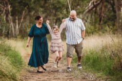 Parents walk along a track and lift their little girl up as she holds their hands