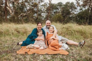 A family sit on a blanket cuddled together in a field of long grass