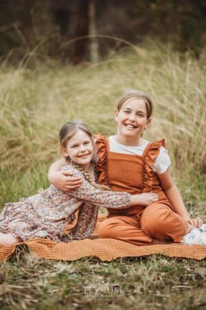 Two sisters sitting on a blanket cuddle each other in a grassy field