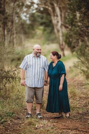 A couple hold hands as they stand on a bush trail and giggle