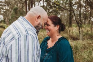 A couple smile as they hug with their foreheads pressed together in a field
