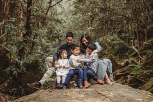Parents tickle their kids as they all sit on a large rock at Lennox Bridge