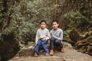 Two little boys sit on a huge rock at Lennox Bridge surrounded by greenery