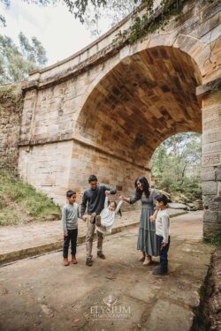 Parents swing their little girl between them as they stand under a sandstone arch