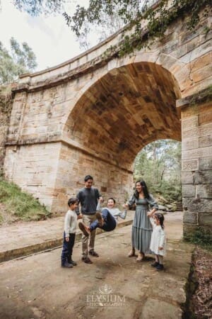 Parents swing their son between them as they stand beneath a sandstone arch