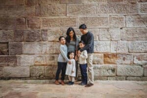 A family stand together cuddling against a sandstone wall at Lennox Bridge