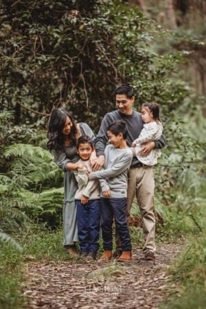 A family tickle their little boy as they stand on a bush track