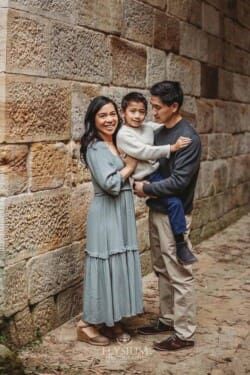 A couple hug their little boy between them as they stand under a stone bridge