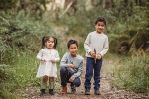 Three siblings stand on a bush track surrounded by trees at Lennox Bridge