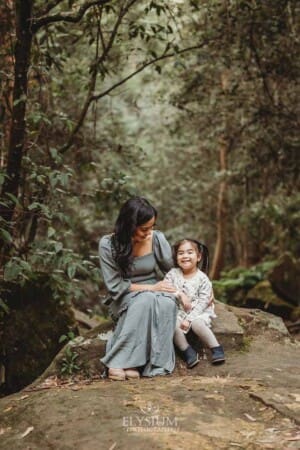 A mother sits on a large rock and hugs her little girl at Lennox Bridge