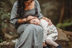 A little girl rests her head in her mothers lap as she strokes her hair
