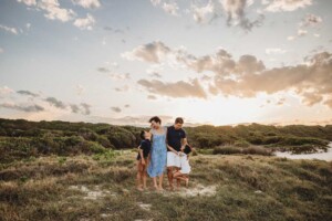 A natural family photograph of parents cuddling their children standing on a Maroubra sand dune with the golden sunset behind them
