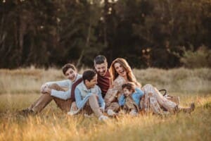 A family sit and laugh naturally in a field of long grass at sunset
