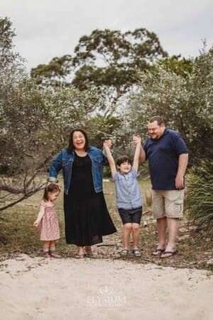 A family walking on a sandy path lift their son between them and laugh