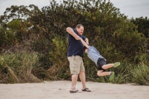 A father swings his son around on a sandy beach