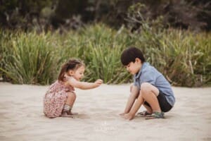 Two siblings crouch on the sand at a beach and play
