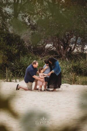 A family stand on a sandy beach and hug each other surrounded by trees