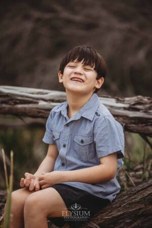A little boy laughs as he sits on a log of driftwood at a beach