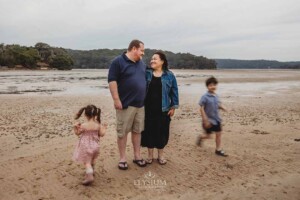 A couple stand on a sandy beach as their two children run around them in a blur