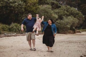 Parents walk along a beach and swing their daughter between them