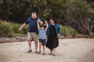 Parents walk along a beach and lift their son between them
