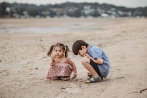 Two siblings crouch on an exposed sand flat and look for crabs at low tide