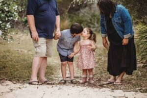 A little boy leans in to kiss his little sister as they stand on a sandy path