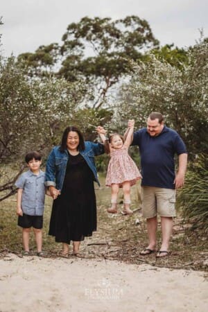Parents lift their little girl between them as they walk along a sandy path