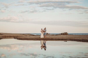 Family photograph of parents holding their small children on a beach with their reflection in a still pool of water