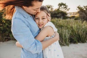 A mother holds her daughter close in a tight hug standing on a beach