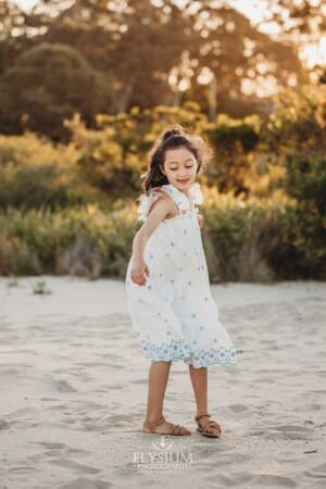 A little girl twirls on the sand as the sun sets behind her over a beach