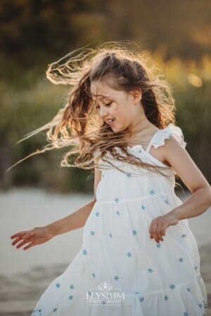 A girl with windswept hair spins in circles on the sand at sunset