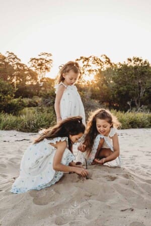 Three little girls on a beach build sandcastles at sunset