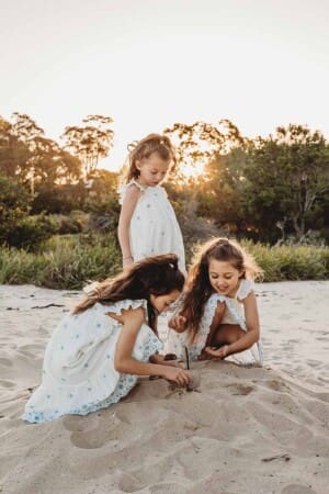 Three little girls play happily in the sand at Cronulla Beach as the sunset turns golden behind them