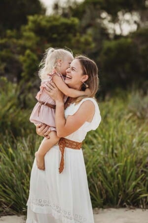 A little girl and her mother giggle and hug as they twirl about in a green field