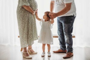 A little girl looks up and pats her pregnant mother on her round belly