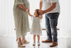 A little girl looks up and pats her pregnant mother on her round belly